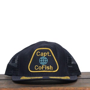 May include: Black mesh trucker hat with a gold and blue embroidered patch that says "Capt. CoFish" and features a globe.