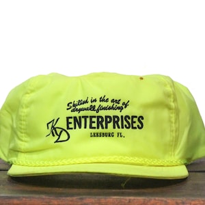 May include: A bright yellow construction worker's hat with black text that reads "Skilled in the art of drywall finishing K ENTERPRISES Leesburg FL."