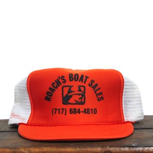 Puede incluir: Gorra de camionero naranja y blanca con el texto "Roach's Boat Sales" y el número de teléfono (717) 684-4810.