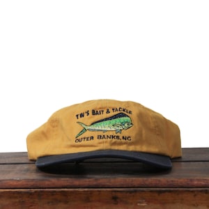 K&ouml;nnte beinhalten: Senfgelbe Kappe mit marineblauem Schirm. Die Kappe zeigt eine gestickte Fischgrafik in Gr&uuml;n und Blau mit dem Text "TW'S BAIT & TACKLE OUTER BANKS, NC" in Wei&szlig;.