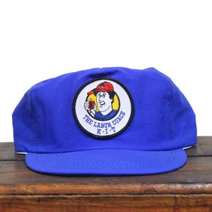 May include: Blue baseball cap with a patch featuring a cartoon character and the text "The Labor Coach K-Y-T".