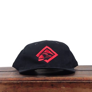 May include: A black baseball cap featuring a red embroidered logo on the front. The logo consists of a diamond-shaped outline containing a stylized graphic of a vehicle or train silhouette. The cap has a structured crown and a curved brim.