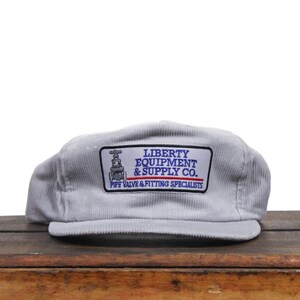 May include: A gray corduroy baseball cap with a white patch that reads "LIBERTY EQUIPMENT & SUPPLY CO. PIPE VALVE & FITTING SPECIALISTS".