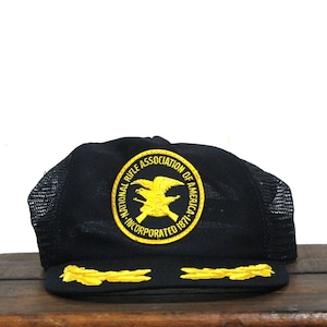 May include: Black mesh trucker hat with a yellow embroidered patch that reads "National Rifle Association of America Incorporated 1871". The patch features an eagle with wings spread and a rifle.