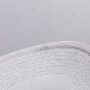 May include: Close-up of the white stitching detail on the underside of a white baseball cap.