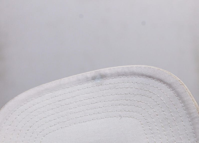 May include: Close-up of the white stitching detail on the underside of a white baseball cap.
