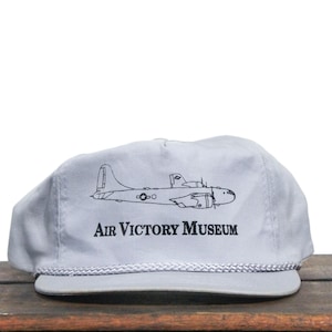 May include: A gray baseball cap with a black outline of a bomber plane and the text "Air Victory Museum".
