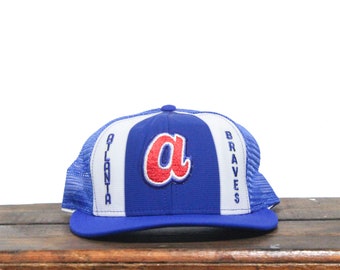 Könnte beinhalten: Eine blaue und weiße Baseballkappe mit einem roten "A" und den Worten "Atlanta Braves" an der Seite.