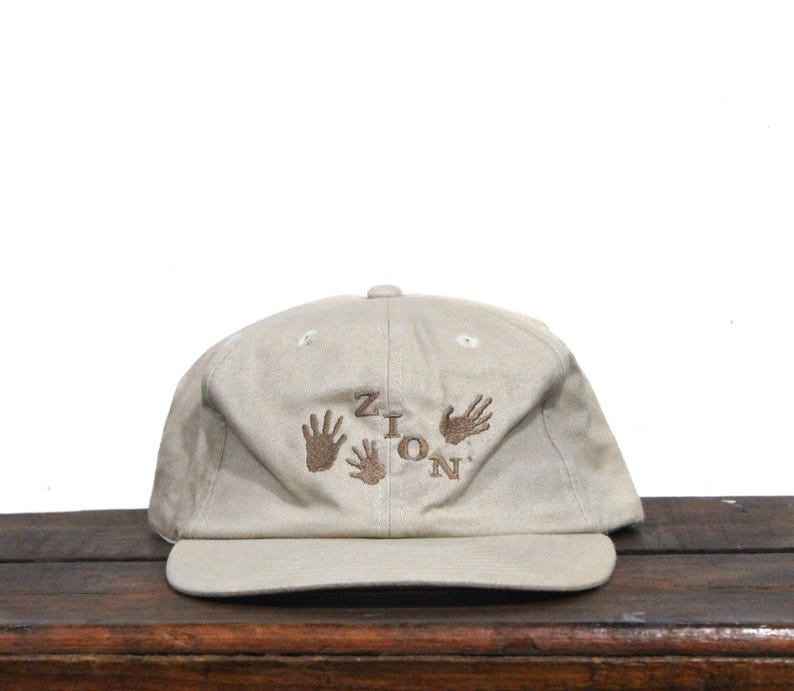 May include: A beige baseball cap with brown embroidery of the word "Zion" and handprints.