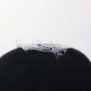 Puede incluir: Primer plano de una gorra de b&eacute;isbol negra con un borde deshilachado blanco. El interior de la gorra es negro y el borde deshilachado es blanco con costuras visibles. El fondo es blanco liso.