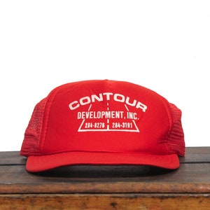 Op de afbeelding: Rode mesh trucker cap met witte geborduurde tekst "CONTOUR DEVELOPMENT, INC. 284-8276 | 284-3181"
