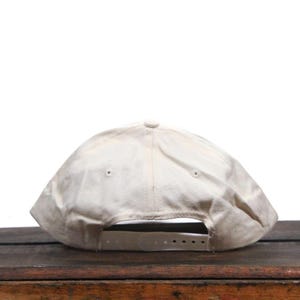 May include: A white baseball cap with a slightly distressed look. The cap has a flat brim and a white adjustable strap.