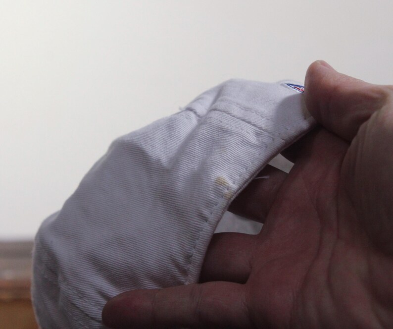 Pu&ograve; includere: Un cappellino da baseball bianco con visiera curva. Il cappellino &egrave; tenuto in mano, mostrando il lato inferiore della visiera e le cuciture interne. Ci sono alcune piccole macchie sul cappellino.