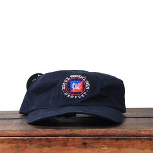 May include: Navy blue baseball cap with the text "2006 U.S. Women's Open Newport" embroidered on the front. The cap has a curved brim and a tag attached to the side.