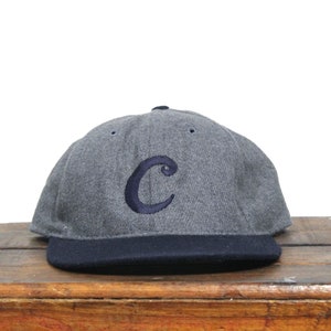 May include: A grey baseball cap with a navy blue brim and a navy blue embroidered letter "C" on the front.