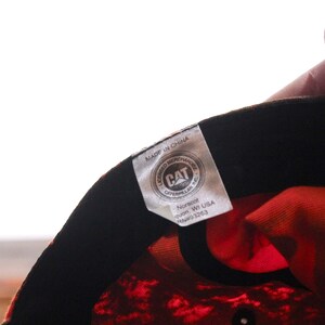 May include: Close-up of a baseball cap's interior, featuring a vibrant orange and black pattern. The cap's lining is a bright orange, and the tag displays the CAT Caterpillar logo and "Made in China".
