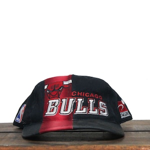 Może przedstawiać: Czarna i czerwona czapka z daszkiem z logo Chicago Bulls i haftowanymi napisami "Chicago Bulls" z przodu.
