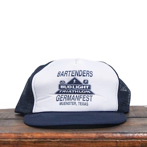 May include: White and blue mesh trucker hat with the text "BARTENDERS BUD LIGHT TRIATHLON GERMANFEST MUENSTER, TEXAS"
