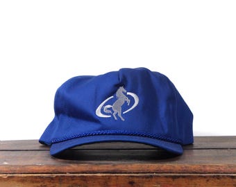 Puede incluir: Gorra de béisbol azul real con un logotipo de caballo bordado en plata. La gorra tiene una visera curva y un detalle de cuerda trenzada en el borde. Fabricada con tejido duradero, adecuada para actividades al aire libre.