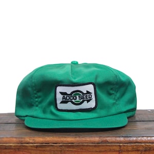 May include: A green trucker hat with a black and white patch that says "ACCO SEED" with a white arrow and a green circle.