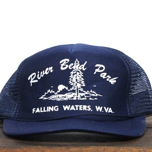 Op de afbeelding: Een donkerblauwe truckercap met een wit geborduurd logo met de tekst "River Bend Park" en "Falling Waters, W.Va."