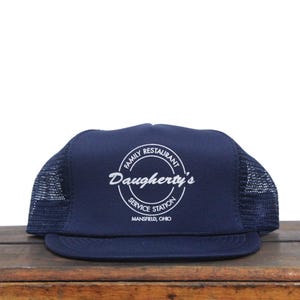 May include: A navy blue trucker hat with a white embroidered logo that reads "Daugherty's Family Restaurant Service Station Mansfield, Ohio".