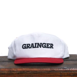 Puede incluir: Gorra de béisbol blanca con visera roja y la palabra "GRAINER" impresa en negro en la parte delantera.