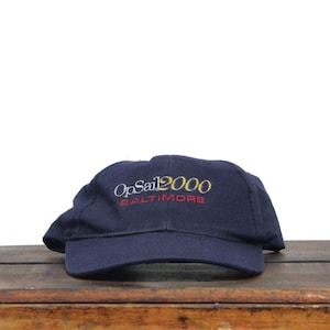 May include: A navy blue baseball cap with the embroidered text "OpSail 2000 Baltimore".