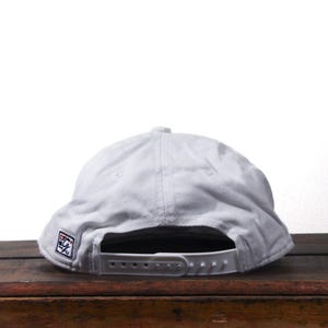 Pu&ograve; includere: Un cappellino da baseball grigio chiaro con visiera piatta e chiusura a scatto regolabile. Il cappellino presenta una piccola toppa ricamata sul lato. Il cappello &egrave; realizzato in un tessuto morbido e resistente.