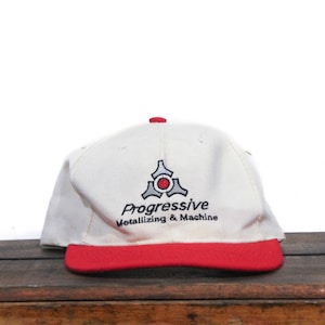 Może przedstawiać: Biało-czerwona czapka z daszkiem z haftowanym z przodu logo "Progressive Metallizing & Machine". Logo przedstawia stylizowany szary trójkąt z czerwonym kołem w środku.