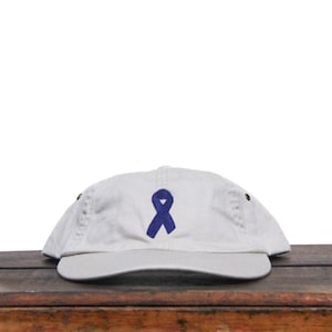 May include: A white baseball cap with a blue ribbon embroidered on the front.