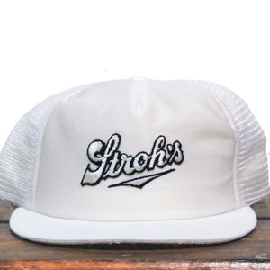 May include: White trucker hat with a black and white embroidered logo that says "Strohs's".