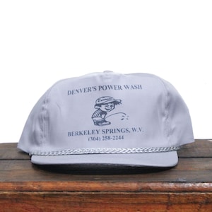 May include: Grey baseball cap with the text "Denver's Power Wash" and a cartoon illustration of a boy. The text "Berkeley Springs, W.V. (304) 258-2244" is also printed on the cap.