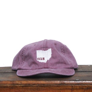 May include: A maroon baseball cap with a white outline of the state of Ohio and the letters "ΠΣΣ" embroidered on the front.