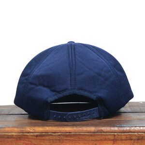 K&ouml;nnte beinhalten: Eine marineblaue Baseballkappe mit flachem Schirm und einfarbiger Farbe. Die Kappe hat einen Klettverschluss hinten.