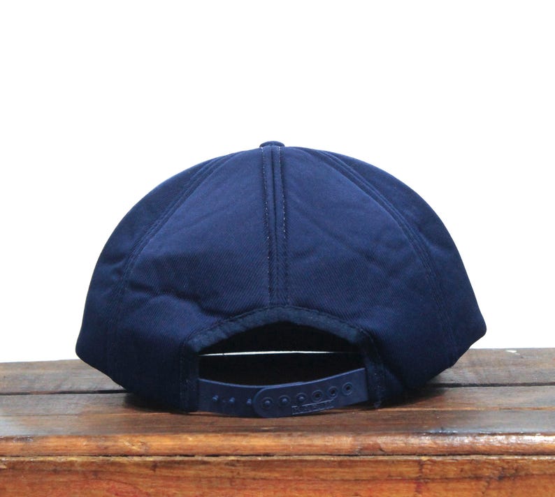 K&ouml;nnte beinhalten: Eine marineblaue Baseballkappe mit flachem Schirm und einfarbiger Farbe. Die Kappe hat einen Klettverschluss hinten.