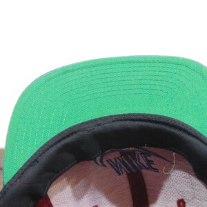 May include: A black and green baseball cap with a purple brim. The cap has a white logo that says "NIKE" on the front.