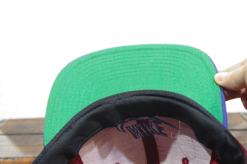 May include: A black and green baseball cap with a purple brim. The cap has a white logo that says "NIKE" on the front.