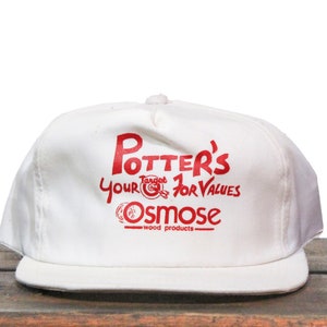 May include: White baseball cap with red text that reads "Potter's Target 1 for Values Osmose - wood products - "