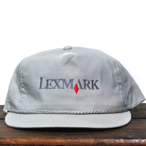 May include: A gray baseball cap with a navy blue embroidered logo that says "LEXMARK" with a red diamond in the middle.