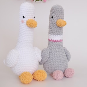 May include: Two crocheted stuffed goose toys. One is white with yellow feet and the other is gray with pink feet.