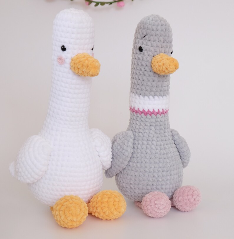 May include: Two crocheted stuffed goose toys. One is white with yellow feet and the other is gray with pink feet.