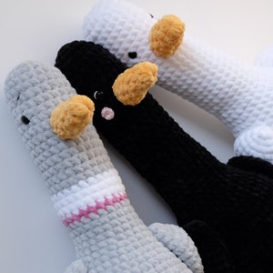 May include: Three crocheted stuffed animal geese in gray, black, and white. The geese have yellow beaks and pink eyes. The gray goose has a white and pink collar.