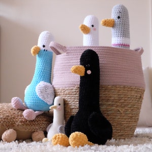 May include: A collection of crocheted bird toys in various colors, including blue, white, black, and gray. The birds are sitting in a woven basket with a pink and brown pattern.