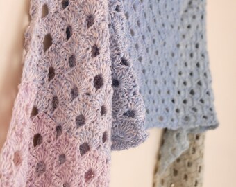 Può includere: Uno scialle all'uncinetto in tonalità lavanda, azzurro e grigio. Lo scialle è realizzato con un delicato motivo a punto aperto.