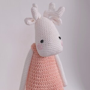 May include: A white crocheted stuffed animal shaped like a moose wearing a pink crocheted dress.