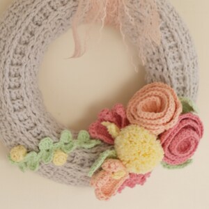Puede incluir: Una corona tejida a mano de color gris, adornada con flores de ganchillo en tonos rosa, amarillo y melocot&oacute;n. Un lazo de tul rosa claro a&ntilde;ade un toque delicado. Un elemento decorativo encantador.