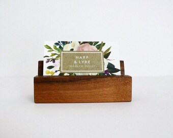 May include: A wooden business card holder with a floral business card that reads "HARP & LYRE modern decor".