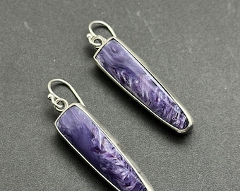 May include: A pair of dangle earrings featuring elongated, rectangular purple stones with swirling patterns, set in silver-toned metal. The earrings have a simple hook design for pierced ears, showcasing a natural, marbled appearance.