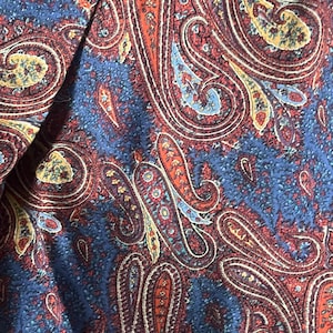 May include: Close-up of a fabric with a paisley pattern. The design features large, ornate teardrop shapes in shades of red, orange, yellow, and blue. The fabric appears to be soft and possibly used for clothing or home decor.